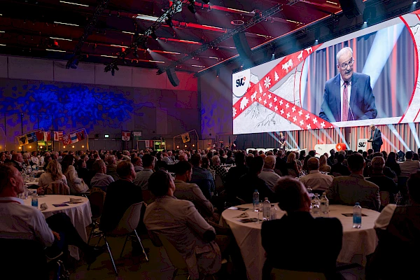 Eventfotograf Festhalle Bern: Redner auf der Bühne, live auf der Grossleinwand mit Wintermotiv übertragen – Gäste verfolgen die Präsentation