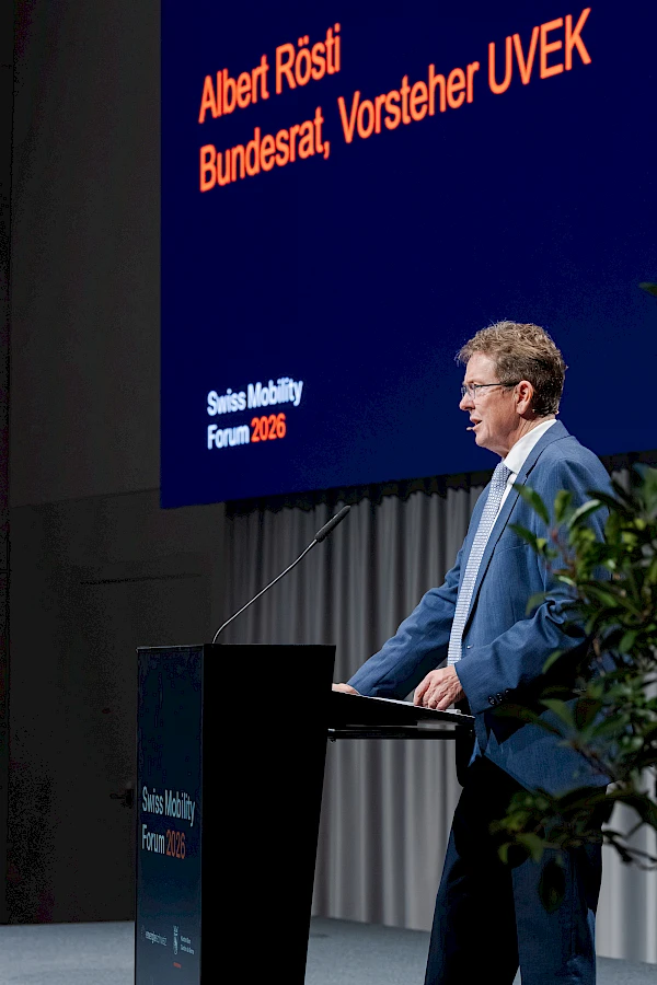 Bildkomposition mit Anspruch: Bundesrat Albert Rösti, Vorsteher UVEK, am Rednerpult – Name und Funktion sauber auf der Leinwand des Swiss Mobility Forum 2026 integriert. So entsteht Redner-Präsenz, die ohne Nachbearbeitung medien- und socialmedia-ready ist.